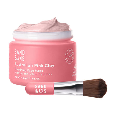 An open tub of Sand & Sky Australian Pink Clay Porefining Face Mask 60g next to a brush