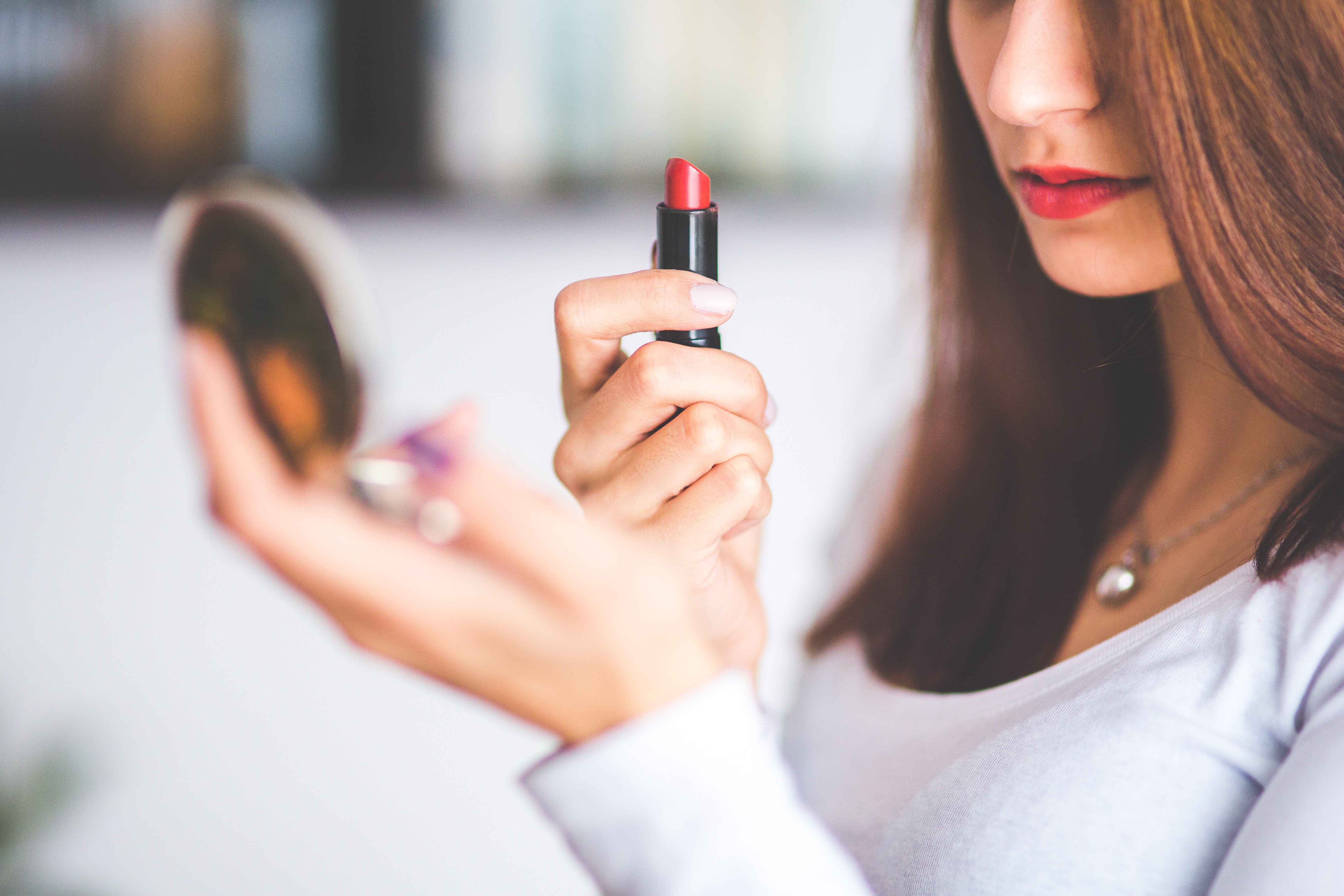 Woman looking at hand mirror about to apply lipstick